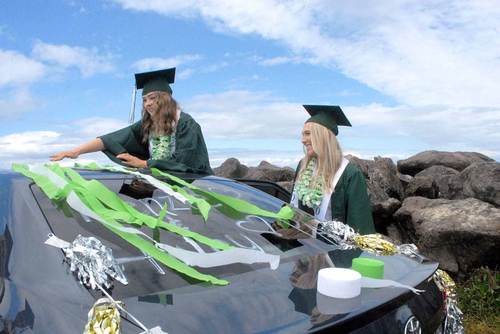 Port Angeles High School seniors Haley Pressley, left, and Bella Money decorate a car with streamers in the schools colors at the start of a graduation procession for the Class of 2020. (Keith Thorpe/Peninsula Daily News)