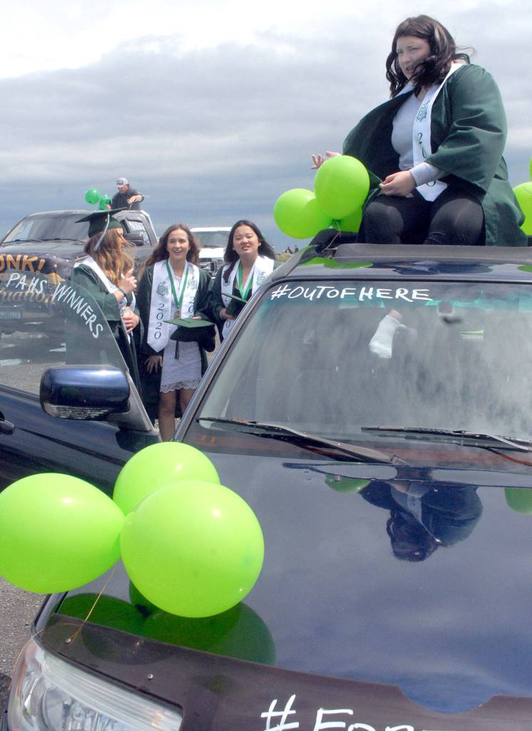 Port Angeles High School senior Camryn Mason sits on top of a car at Ediz Hook prior to the start of a processional motorcade of graduates as classmates, from left, Madilyn Roenig, Nacia Bohman and Felicia Che stand nearby Friday. (Keith Thorpe/Peninsula Daily News)