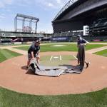 Grounds crew workers Jacob Weiderstrom, left, and Marcus Gignac pull a tarp off home plate as they continue to keep the Seattle Mariners field in playing shape as the ballpark goes into its seventh week without baseball played because of the coronavirus outbreak Monday, May 11, 2020, in Seattle. A person familiar with the decision tells The Associated Press that Major League Baseball owners have given the go-ahead to making a proposal to the players union that could lead to the coronavirus-delayed season starting around the Fourth of July weekend in ballparks without fans. (AP Photo/Elaine Thompson)