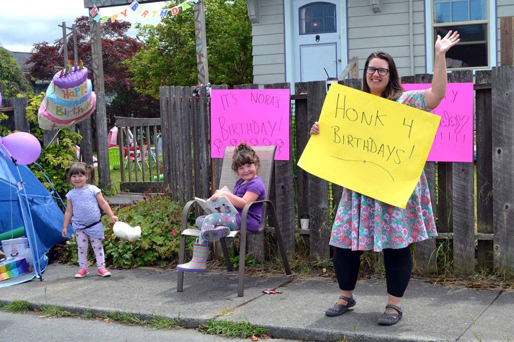 Mom Wynn Hannam holds a sign for drivers to honk for her daughter Noras third birthday. Nora, left, waved to cars with her sister, Ellie, mom, and dad, Jared, not pictured. (Matthew Nash/Olympic Peninsula News Group)