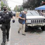 A Seattle police officer asks people to move aside to allow police vehicles through as investigators, right, look over a car involved in a shooting Monday in Seattle, where streets are blocked off in what has been named the Capitol Hill Occupied Protest zone. (Elaine Thompson/The Associated Press)
