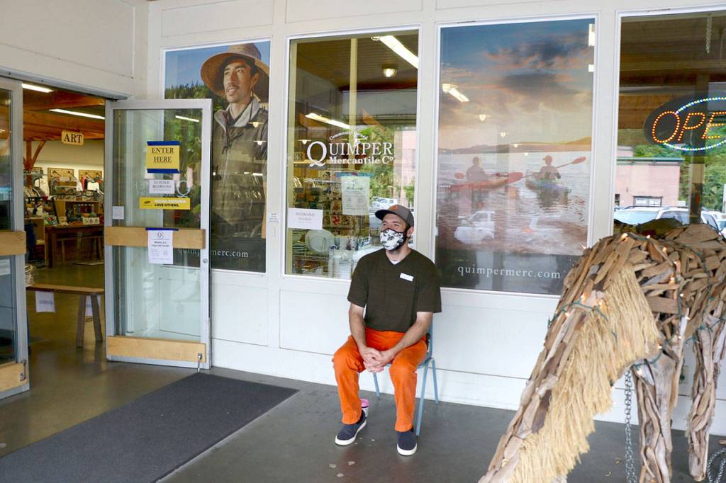 A Quimper Mercantile employee sits outside the shop to act as a greeter and encourage customers to wear masks and use hand sanitizer. (Ken Park/Peninsula Daily News)