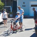 With Cherry Bibler, Sequim School District physical therapist, left, and Sequim Noon Rotary member Bob Macaulay, right, looking on, 11-year-old Abby Johnson takes a rides on her adaptive bike  with new steering bar  with help from her father, Alvin Pitts. (Photo by Doug Schwarz)