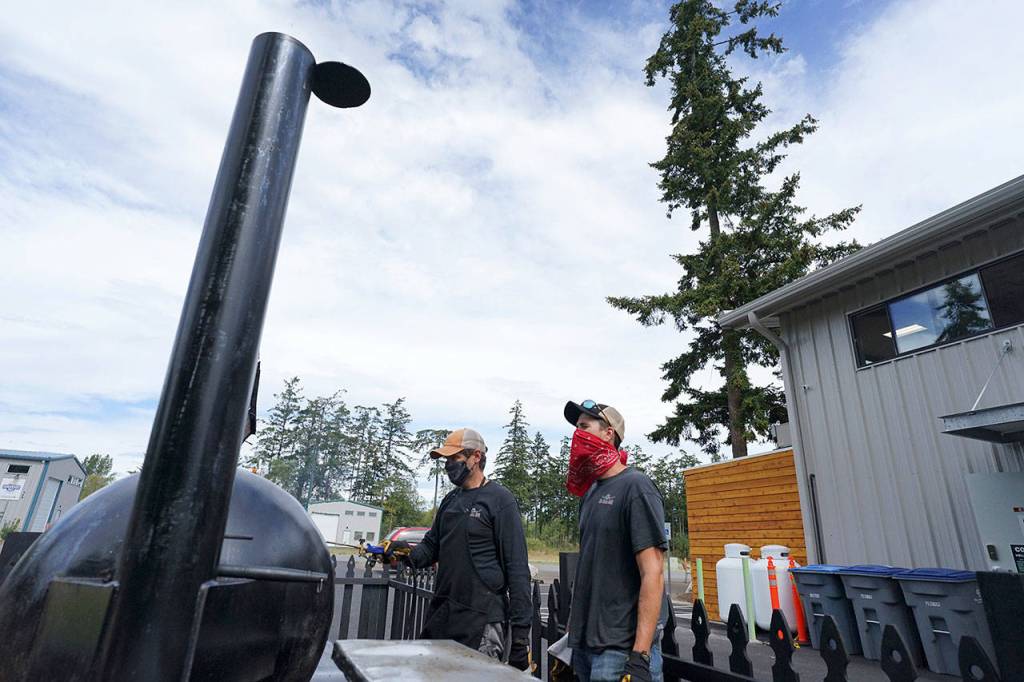Mike Harbin of Mo-Chilli BBQ shows apprentice pitmaster Cody Taylor how to properly clean a smoker Thursday outside Lilas Kitchen in Port Townsend. (Nicholas Johnson/Peninsula Daily News)