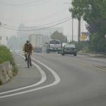 A cyclist travels along Water Street on Saturday morning as the iconic Hastings Building in downtown Port Townsend is shrouded in smoke in the background. (Nicholas Johnson/Peninsula Daily News)