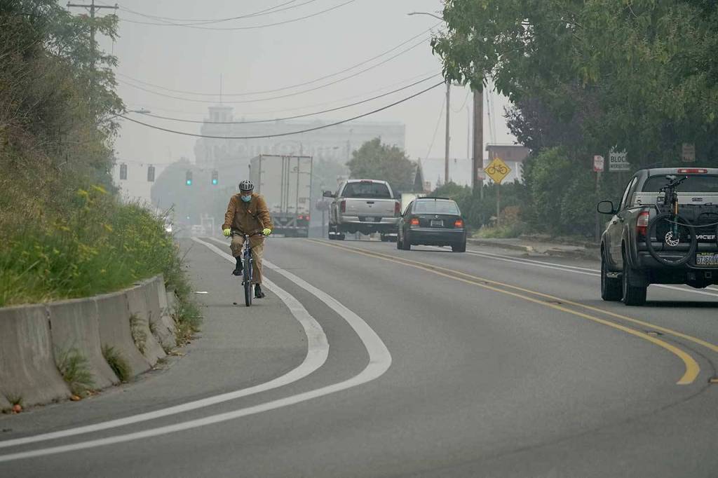 A cyclist travels along Water Street on Saturday morning as the iconic Hastings Building in downtown Port Townsend is shrouded in smoke in the background. (Nicholas Johnson/Peninsula Daily News)