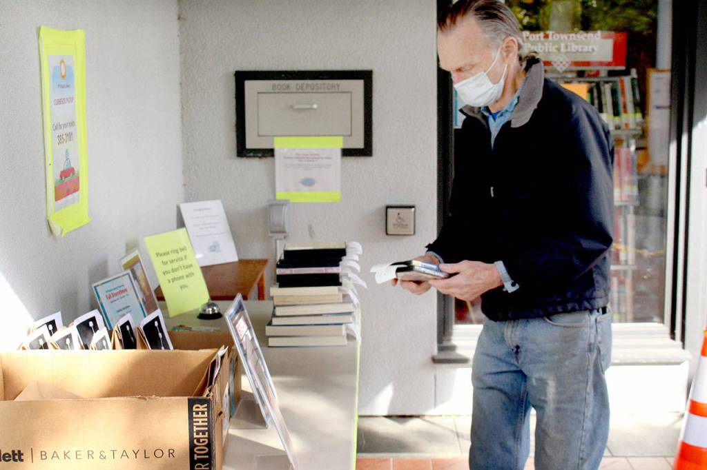 Sidney Collins of Port Townsend picks up DVDs from the hold table outside of the Port Townsend Public Library on Tuesday, Oct. 20, 2020, as part of the librarys curbside pickup system. (Zach Jablonski/Peninsula Daily News)