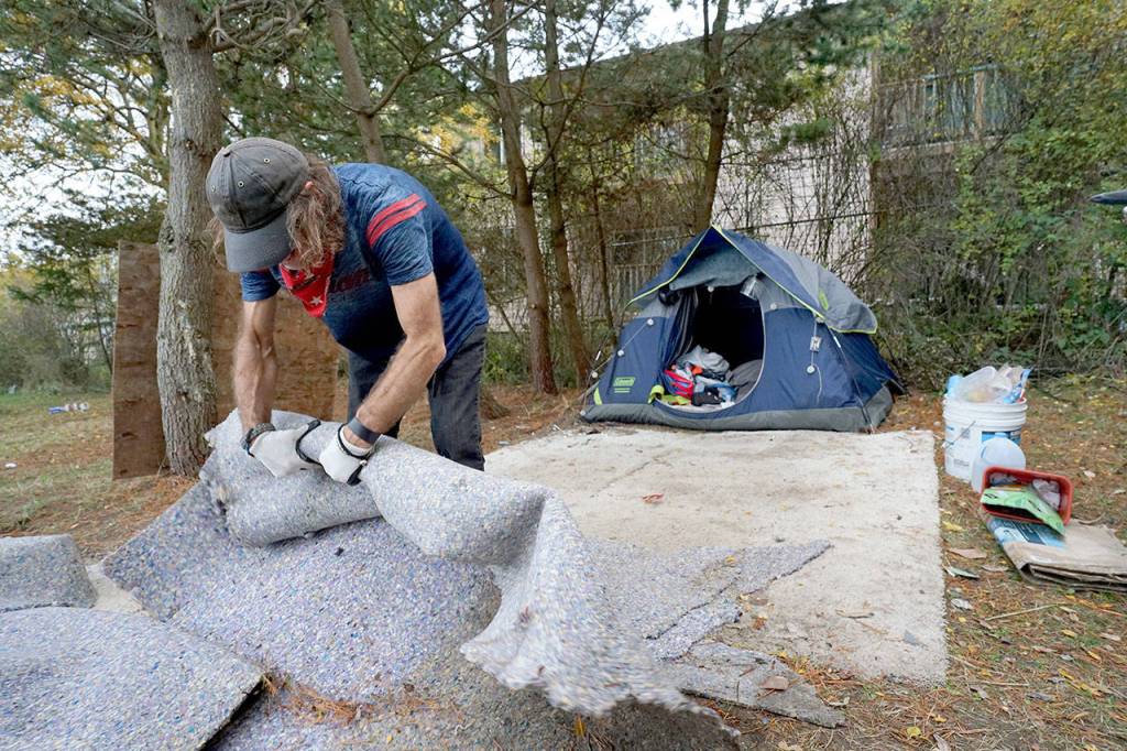 Daniel Overbey cleans up his campsite Nov. 4, which sits across a chainlink fence from an apartment complex, in order to move to another spot at the Jefferson County Fairgrounds campground in Port Townsend. (Nicholas Johnson/Peninsula Daily News)