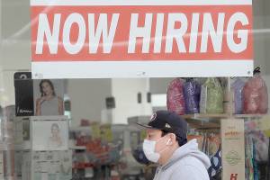 FILE - This May 7, 2020, file photo shows a man wearing a mask while walking under a Now Hiring sign at a CVS Pharmacy during the coronavirus outbreak in San Francisco.  On Thursday, Nov. 12, the number of people seeking unemployment benefits fell last week to 709,000, the fourth straight drop and a sign that the job market is slowly healing. The figures coincide with a sharp resurgence in confirmed viral infections to an all-time high above 120,000 a day.  (AP Photo/Jeff Chiu, File)