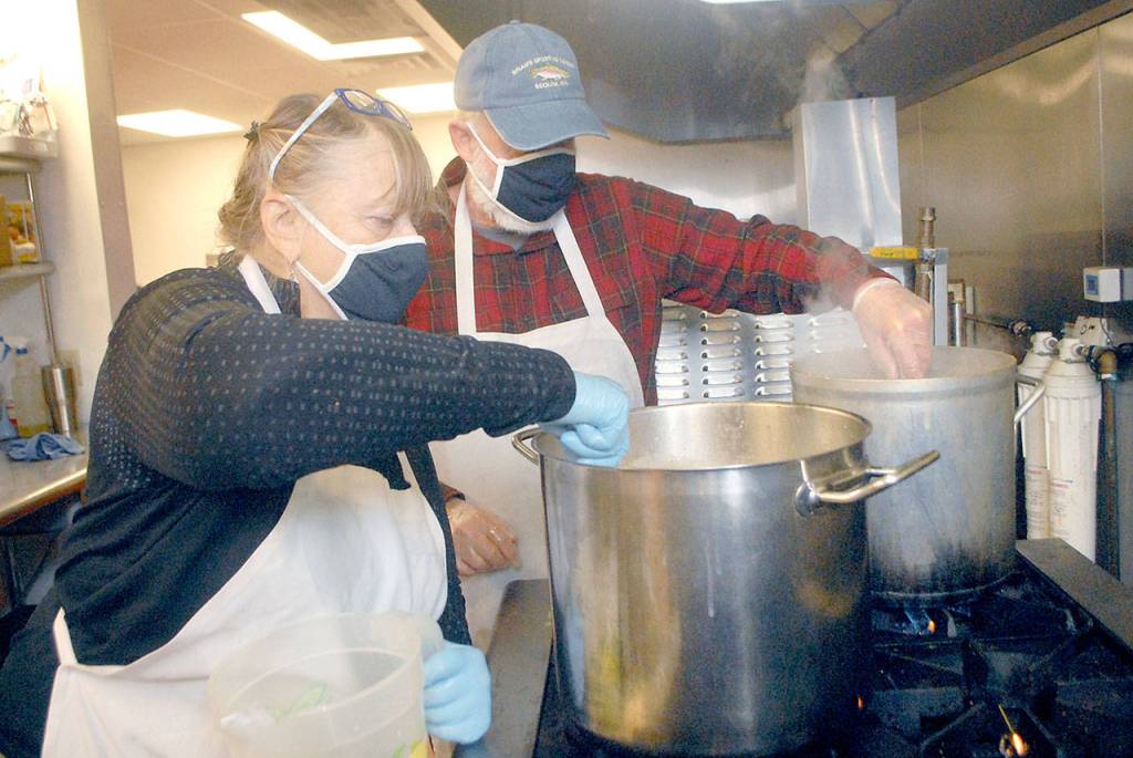 Volunteers Linda and Doug Crabb of Sequim stir pots of gravy in the Salvation Army food kitchen Wednesday, Nov. 25, 2020, in Port Angeles. (Keith Thorpe/Peninsula Daily News)