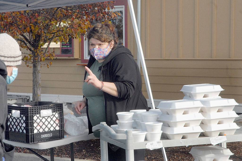 Sendy Alvarez, manager of Hardys Market, takes a dinner order outside the Sequim convenience store and deli on Thanksgiving Day. In an annual tradition, the market gave away traditional turkey dinners to people, foregoing inside service this year in favor of walk-up delivery to adhere to COVID-19 distancing guidelines. (Keith Thorpe/Peninsula Daily News)
