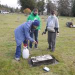 Jan Urfer, secretary with the Michael Trebert Chapter of the Daughter of the American Revolution, works with scouts Hunter Halverson and Cayden Beauregard from Sequim Troop 90 to clean headstones and grave markers at Sequim View Cemetery on Nov 28. Members of the chapter and scout troop were busy preparing the cemetery for a Wreaths Across America event slated for Dec. 19. (Michael Dashiell/Olympic Peninsula News Group)
