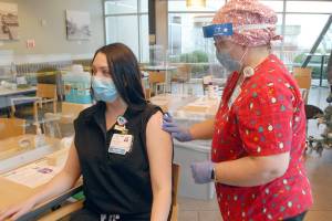 Keith Thorpe/Peninsula Daily News
Registered nurse Gretchen Souza, director of education at Olympic Medical Center, right, applies a bandage to emergency services nurse Samantha Counts, who was the first person in Clallam County to receive a vaccination against COVID-19 during a clinic at the Port Angeles hospital on Friday.