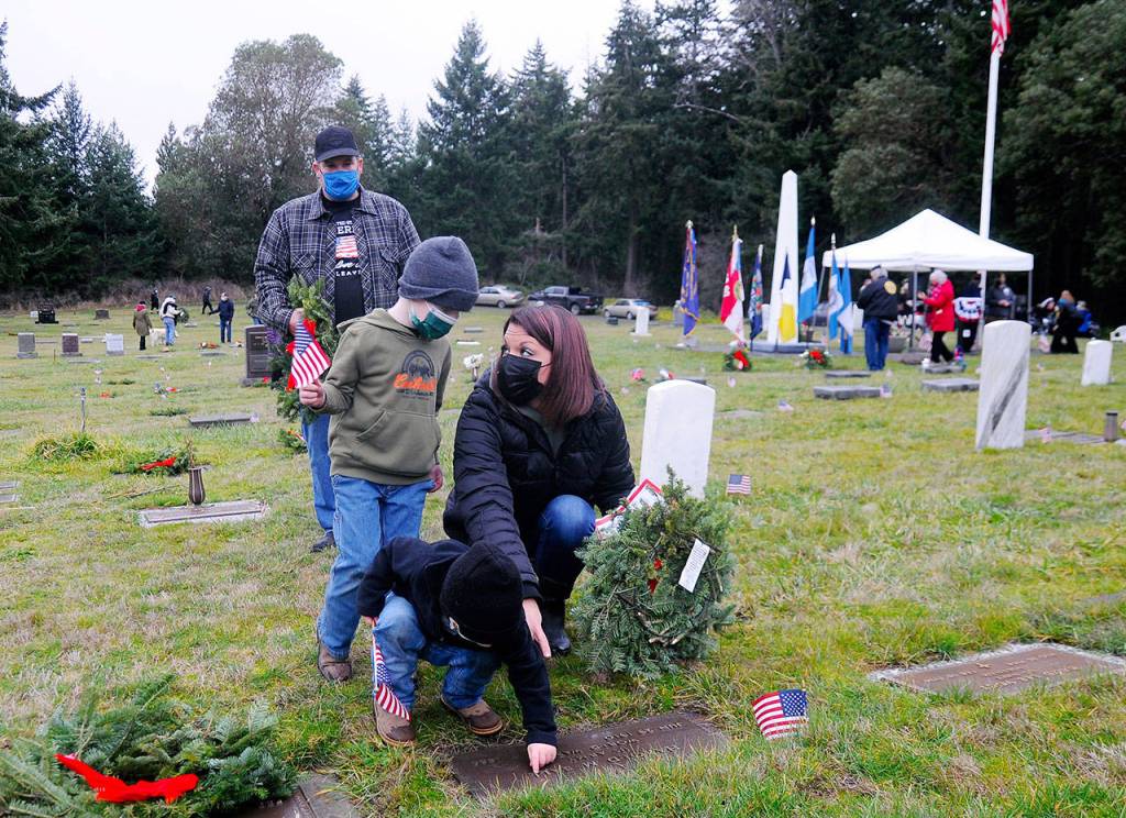 Jennifer Groves of Port Angeles helps sons Blake, 5 (standing), and 2-year-old Bryce, place a wreath on a veterans grave marker Saturday, as Groves stepfather Bobby Yaun looks on. Groves said she attended the event to teach my men to show honor. (Michael Dashiell/Olympic Peninsula News Group)