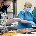 Volunteers Mya Lindstrom, left, and Judy Robinett direct the carrots and scalloped potatoes through the assembly line during the Tri-Area Community Center's Christmas dinner on Friday. Diane Urbani de la Paz/Peninsula Daily News