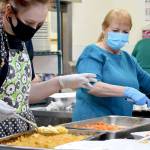 Volunteers Mya Lindstrom, left, and Judy Robinett direct the carrots and scalloped potatoes through the assembly line during the Tri-Area Community Centers Christmas dinner on Friday. (Diane Urbani de la Paz/Peninsula Daily News)