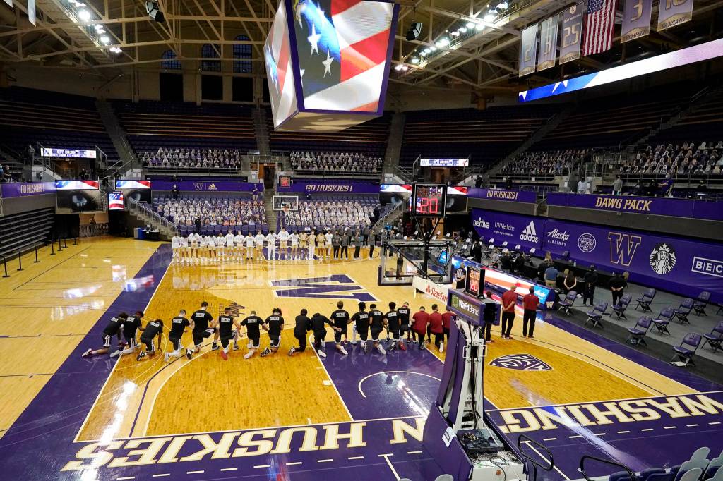Washington State players kneel on the court as Washington players stand in an otherwise nearly empty Hec Ed Arena during the singing of the national anthem before an NCAA college basketball game Sunday, Jan. 31, 2021, in Seattle. (AP Photo/Elaine Thompson)
