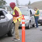 Volunteers Anthony Brigandi and Jennifer Rogers check out the next cars in line for their appointment to get a COVID-19 Pfizer vaccine Saturday morning at the Port Angeles High School campus. The whole process at the PAHS auxiliary gym and adjacent parking lot is run smoothly by over 60 volunteers from across the county and takes about 30 minutes. (Dave Logan/For Peninsula Daily News)