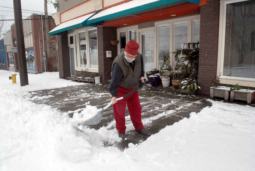 Steve Card, owner of Wild Card Guitars, clears snow from the sidewalk in front of his business on North Oak Street in downtown Port Angeles on Saturday. (Keith Thorpe/Peninsula Daily News)
