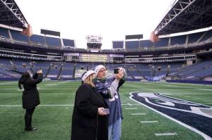 Tom Gallagher, right, wears a Seattle Seahawks jersey and holiday hat as he takes a photo with his wife Debbie on the turf at Lumen Field, Thursday, Feb. 18, 2021, in Seattle. The couple, who are Seattle Seahawks season ticket holders, were celebrating their 45th anniversary by taking part in the "Field To Table" event at the Seahawks' home stadium on the first night of several weeks of dates that offer four-course meals cooked by local chefs and served at socially distanced tables in an open-sided tent on the field as a precaution against the COVID-19 pandemic. (AP Photo/Ted S. Warren)