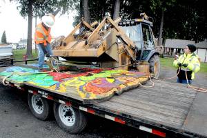 Port Angeles Parks and Recreation worker Darryl Anderson, left, signals to bulldozer operator Leon Leonard as fellow employee Brooke Keohokalole curls up a guide rope after the dragon mosaic from the Dream Playground at Erickson Playfield is lowered onto a trailer earlier this week in Port Angeles. Demolition has begun on the mostly wooden playground, originally built by volunteer labor in September 2002, to make way for modernized playground equipment later this year. The dragon, which once had a playground slide coming from its nose, will be put into storage and later incorporated into the new playground. (Keith Thorpe /Peninsula Daily News)