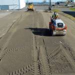 Richard Brandt of Lakeside Industries uses a steam roller on a layer of sand Thursday to create a level surface that will become the base for a temporary ice skating rink in a city parking lot along Front Street in downtown Port Angeles. The rink will be the centerpiece for the annual Port Angeles Ice Village, which would normally be held in the winter months, but was moved to spring because of restrictions imposed by COVID-19. Skating is scheduled to begin on March 19 and run through April 18. (Keith Thorpe/Peninsula Daily News)