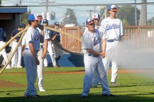 Members of the Port Angeles Lefties baseball team, including assistant coach Anthony Murillo, holding a hose, water down the infield prior to the start of Tuesday evenings season opener against the Highline Bears at Port Angeles Civic Field. (Keith Thorpe/Peninsula Daily News)