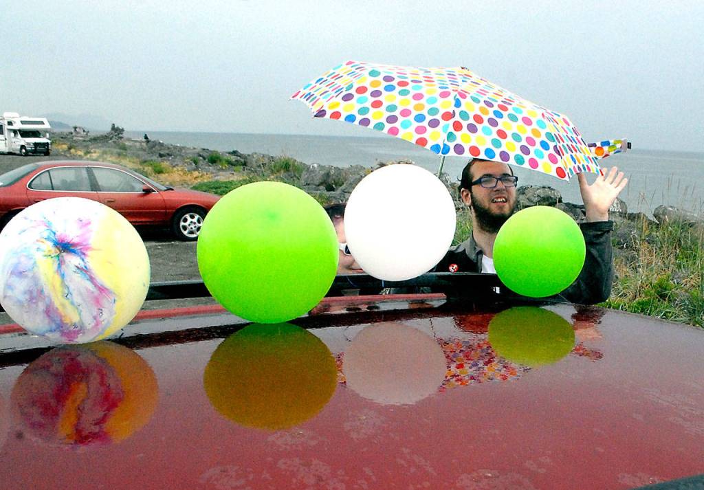 Port Angeles High School graduate Hunter Gorss holds an umbrella as his mother, Jamie Gorss, ties balloon to their vehicle during a rain shower at the start of Fridays Senior Parade. (Keith Thorpe/Peninsula Daily News)