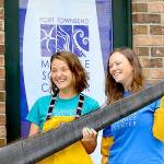 Holding a piece of baleen from a bowhead whale, Port Townsend Marine Science Center exhibit and outreach specialist Mandi Johnson, left, and aquarium specialist Marley Loomis stand before the centers newly acquired Flagship Landing building in downtown Port Townsend. (Diane Urbani de la Paz/Peninsula Daily News)