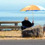 Kathleen Krecklow sits under an umbrella as she converses with Jo Ehly on the shore of Dungeness Bay at Dungeness Landing County Park on Wednesday. The women, both of Sequim, were sharing the morning with other friends in a weekly gathering. (Keith Thorpe/Peninsula Daily News)