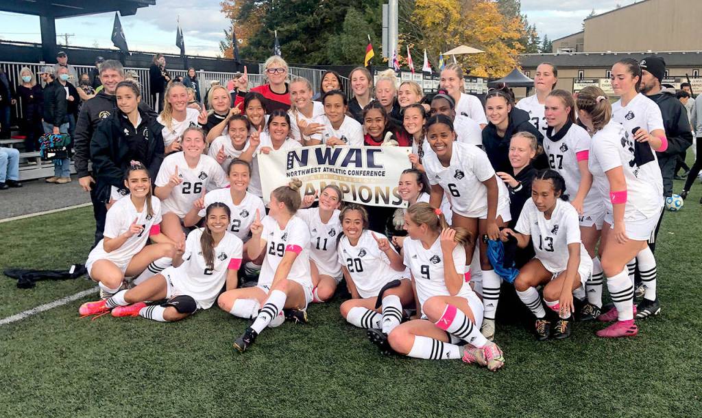 Members of the Peninsula College womens soccer team gather around the NWAC North Region championship banner after clinching the top spot in the division with Wednesdays win over Skagit Valley. (Keith Thorpe/Peninsula Daily News)
