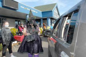 Kayleen McDonald of the Sequim unit of the Boys & Girls Clubs of the Olympic Peninsula delivers bagged lunches to a waiting car as unit director Tessa Jackson, left, looks on during a drive-thru Halloween in front of the organizations Sequim facility last year. Besides lunch bags, trick-or-treaters were offered hats, treats and coloring books. (Keith Thorpe/Peninsula Daily News)