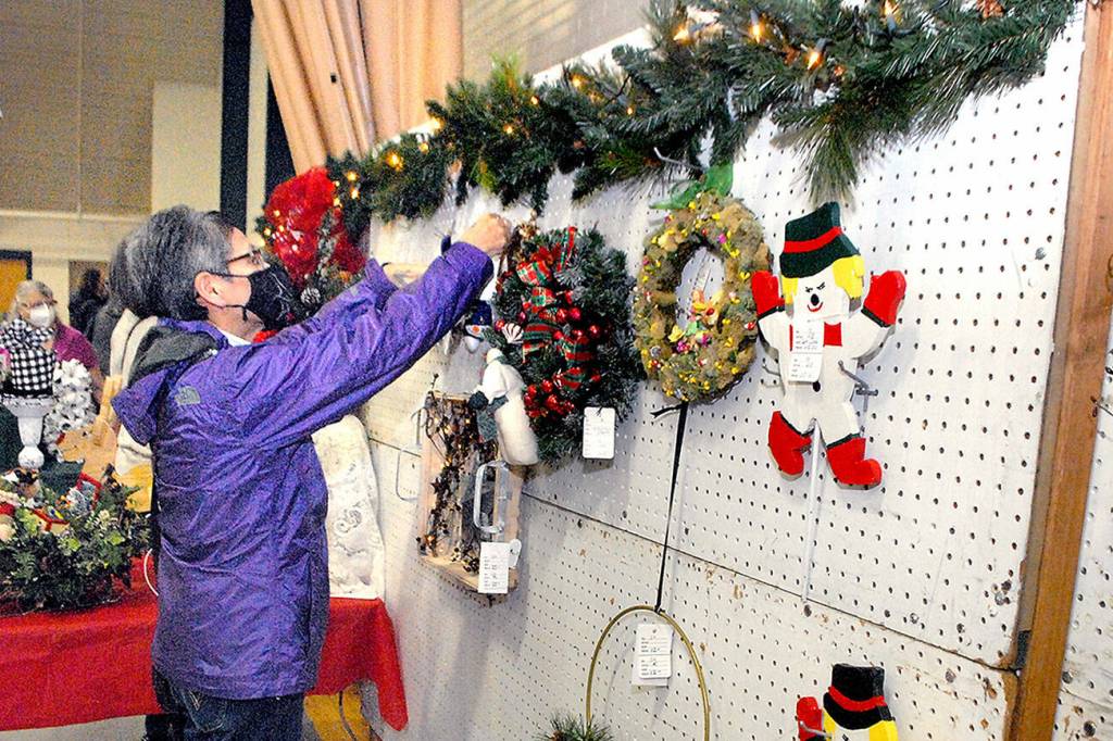 Marla Tolliver of Neah Bay examines wreaths and hanging holiday decorations on Saturday at the annual Christmas Cottage craft fair at Vern Burton Community Center in Port Angeles. The free event, which continues Sunday from 10 a.m. to 4 p.m., features a wide variety of holiday crafts created by a collection of local artists and artisans. (Keith Thorpe/Peninsula Daily News)
