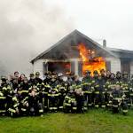 Firefighters and medics from Clallam County Fire District 2 pose for photos in front of a flaming house, part of a training exercise on Sunday at 2354 E. Fifth Ave. in the Gales Addition east of Port Angeles. The burn of the donated house allowed firefighters to hone their skills in a live-fire scenario through two days of training sessions. Once extinguished, the site will be cleared to make way for future development. (Keith Thorpe/Peninsula Daily News)