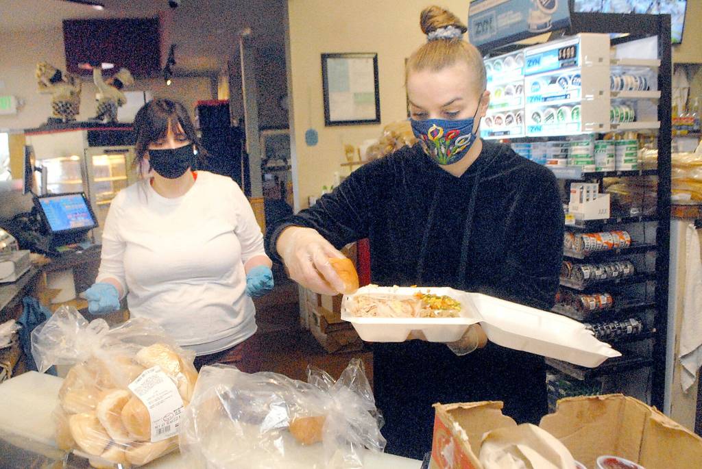 Volunteer Tenisha Towless, front, assembles a carry-out Thanksgiving meal as fellow volunteer Sarah Gaylord waits to distribute it to a hungry guest on Thursday at Hardys Market in Sequim. The market and deli planned to give away about 200 free meals as part of their annual Thanksgiving tradition. (Keith Thorpe/Peninsula Daily News)