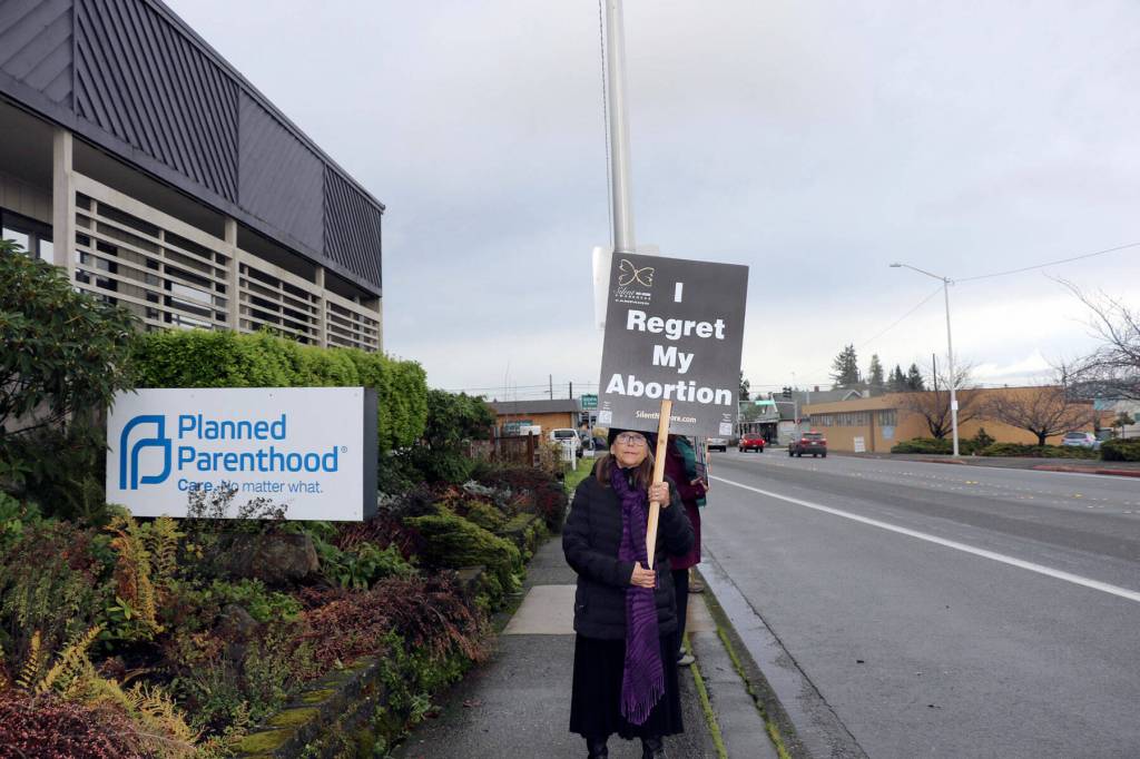 Kathy Gonzales holds a sign saying she regrets getting an abortion. (Ken Park/Peninsula Daily News)