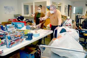 Deseree Garza, a representative of First Federal, left, and Salvation Army Major Ron Wehnau assemble bundles of Christmas presents for the organizations Angel Tree program on Tuesday at the Salvation Army Community Center in Port Angeles. Major Barbara Wehnau said 201 families representing more than 500 children would be given packages of presents for the 2021 holiday season. (Keith Thorpe/Peninsula Daily News)