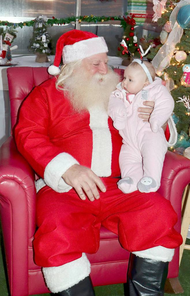 Barry Swegle plays Santa at the Candy Cane Christmas Cabin at The Answer for Youth (RAFY) Sprouting Hope Greenhouse as he holds 4-month-old Persephanie Svilar of Port Angeles. (Dave Logan/for Peninsula Daily News)