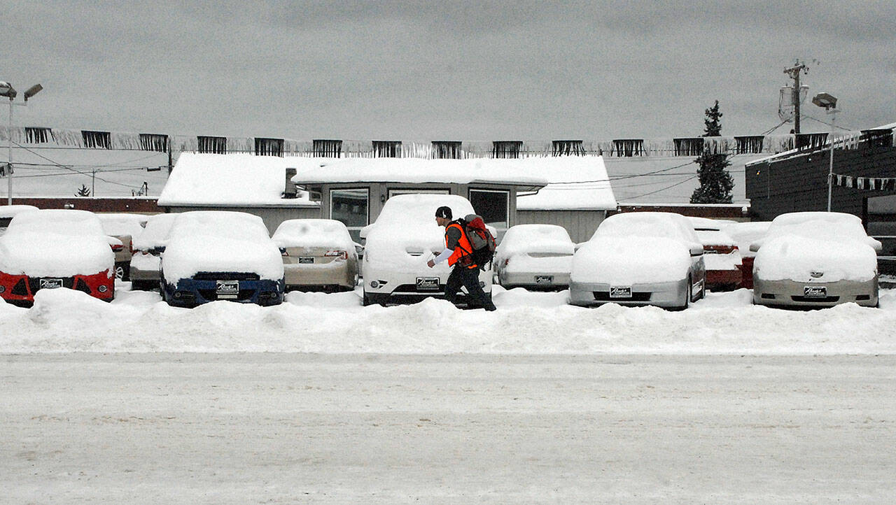 A pedestrian walks past a line of snow-covered vehicles on the lot of Randys Auto Sales in the 800 block of East First Street in Port Angeles on Tuesday. A small amount of overnight snow added to previous snowfalls that began on Christmas Day along most of the North Olympic Peninsula. (Keith Thorpe/Peninsula Daily News)