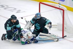 Seattle Kraken goaltender Philipp Grubauer, right, makes a stop as Kraken defenseman Adam Larsson (6) and Vancouver Canucks center Matthew Highmore (15) crash against him during the second period of an NHL hockey game Saturday, Jan. 1, 2022, in Seattle. (AP Photo/Ted S. Warren)
