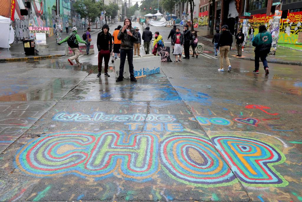 FILE - A sign on the street reads "Welcome to the CHOP" as protesters stand near barricades at the CHOP (Capitol Hill Occupied Protest) zone in Seattle on Tuesday, June 30, 2020. An investigation by the city's police watchdog shows Seattle Police exchanged detailed fake radio transmissions about a nonexistent group of menacing right-wing extremists at a crucial moment during 2020 racial justice protests. Officials said fabricating the group of Proud Boys violated department policies. (AP Photo/Ted S. Warren, File)