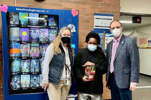 Principal Kristen Lunt (left), Student Lyndel Atwater, and Superintendent Marty Brewer. Lyndel who earned his token for the Inchy Bookworm Vending Machine by cleaning up sporting equipment after a football game without having to be asked.