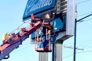 Dana Johnson of Esco Pacific Signs of Chehalis changes light bulbs and performs other maintenance on the Ruddell Auto Mall sign at the intersection of U.S. Highway 101 and Golf Course Road. (Dave Logan/for Peninsula Daily News)
