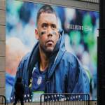 A pedestrian walks past a photo of Seattle Seahawks quarterback Russell Wilson at Lumen Field, Tuesday, March 8, 2022, in Seattle. The Denver Broncos agreed to send a massive haul of players and draft picks to the Seattle Seahawks in a trade for Wilson, two people familiar with the negotiations confirmed to The Associated Press on Tuesday. The blockbuster trade, which is pending Wilson passing a physical, cant become official until the start of the new league year on March 16, 2022. (Ted S. Warren/The Associated Press)