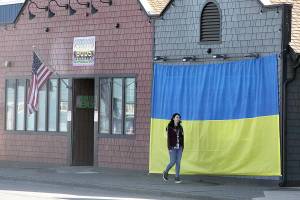 Shawna Small walks on Marine Drive in Port Angeles past a large Ukrainian flag on the outside of Mister Buds, which owner Malik Atwater put up recently along with the U.S. flag he has flown for many years. The flag was hand-sewn by Vivian Wai, Atwaters wife, after the two discussed how to support the Ukrainians as they fight against the invasion of the country launched by Russia on Feb. 24. We felt helpless to do anything to help, Atwater said, adding that it was Wai who came up with the idea. (Dave Logan/for Peninsula Daily News)