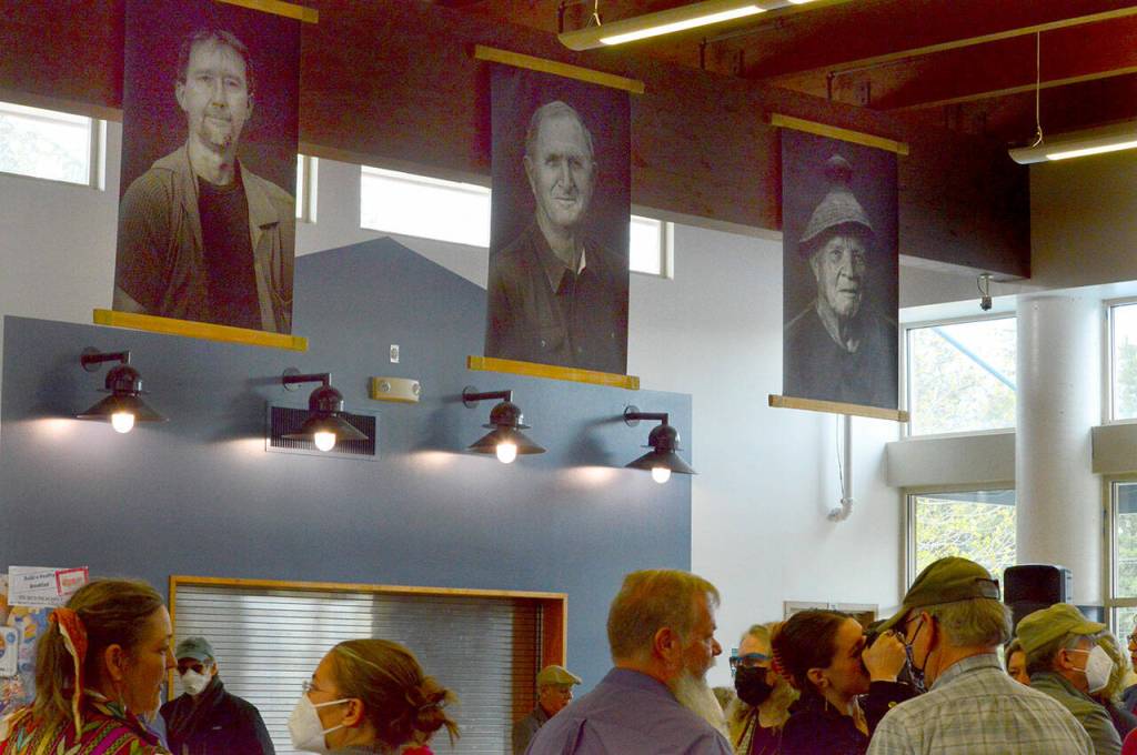 Above the crowd at the opening of the Still Here exhibit at the Chimacum School Commons are Brian Goodmans portraits of, from left, Garold Pomeroy, Ronald Meyer and Ralph Meyer. (Diane Urbani de la Paz/Peninsula Daily News)