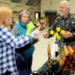 Keith Thorpe/Peninsula Daily News
Cari Gavin, left, and Pam Wennerberg, both of Port Angeles, examine a cutting board created by Tim Smith of Port Angeles-based Blacktail Trail LLC,  right, during Saturday's Mother's Day Market at Vern Burton Community Center in Port Angeles. The event featured a variety of vendor displays with items created mostly by local artisans.