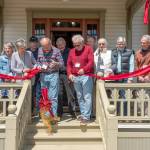 <address>Chair of the Board Christine Satterlee, left, holds the ribbon as Project managers David Satterlee, left, and Chuck Thrasher wield scissors to cut the ribbon to signal the restoration of the 130 year old Worthington House is complete and open to the public. The cutting took place in Quilcene on Friday. (Steve Mullensky/for Peninsula Daily News)</address>