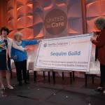 Ann Shanahan, a trustee with the Seattle Childrens Guild Association, presents a banner displaying the Chairmans Award to Sequim Guild President Kathy Bare and Secretary Lydia Stanhope at the Seattle Childrens Guild Association 2022 Annual Meeting & Luncheon on May 13. (Courtesy photo)