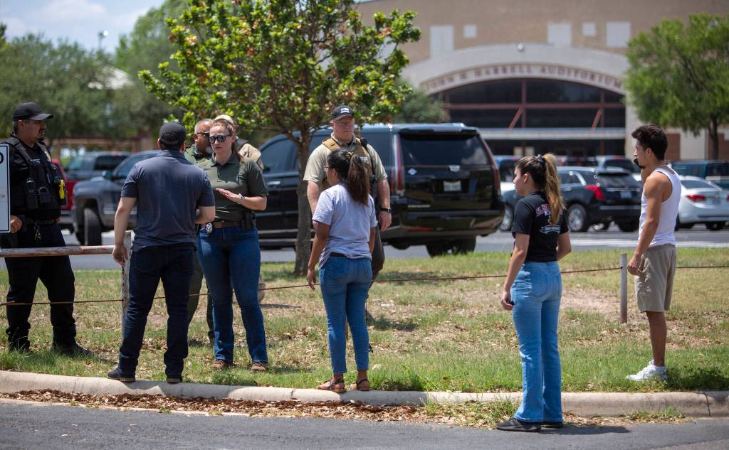 A law enforcement officer speaks with people outside Uvalde High School after shooting a was reported earlier in the day at Robb Elementary School on Tuesday in Uvalde, Texas. (William Luther/The San Antonio Express-News via AP)